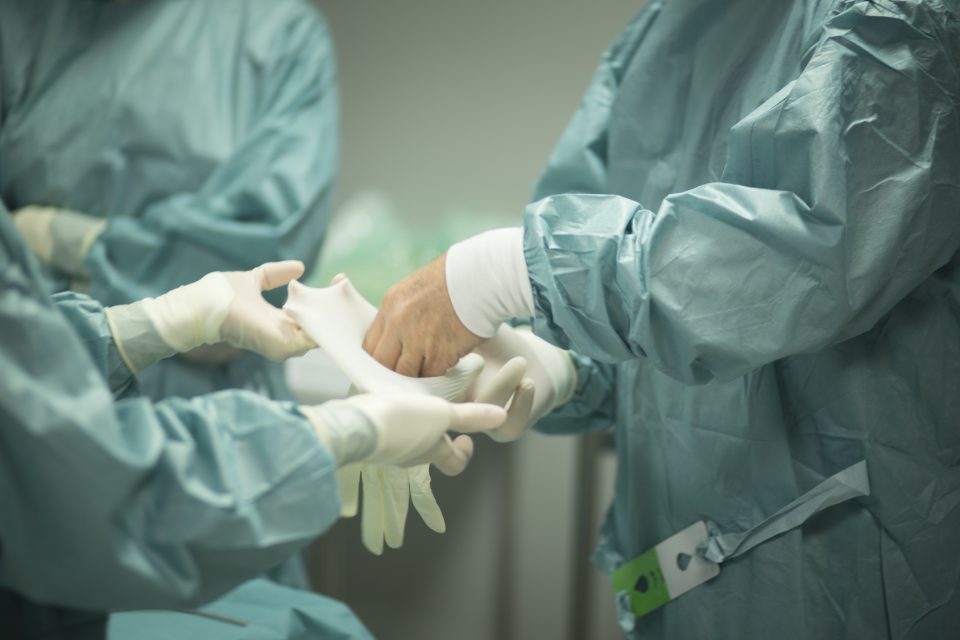 Surgeon in hospital surgery putting on gloves in sterile uniform "scrubs" in operating theater emergency room in surgical operation.