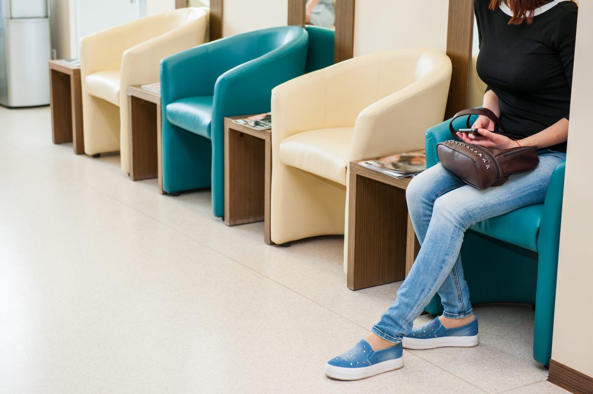 Young girl sitting in waiting room on the one of row of blue and ivory chairs in hall. Selective focus. Medicine, business concept