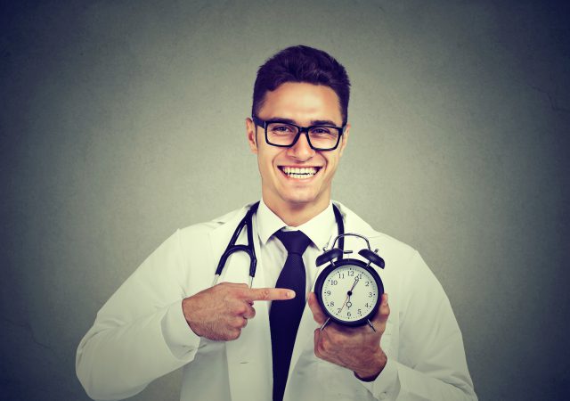 Doctor pointing at alarm clock over gray background