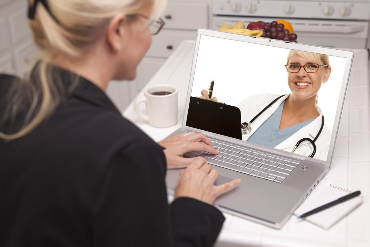Woman In Kitchen Using Laptop - Online Chat with Nurse or Doctor on Screen.