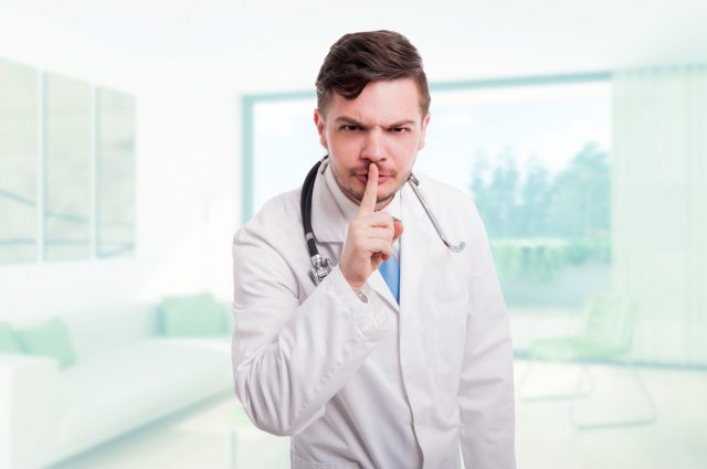 Serious male doctor indicate to keep silence or doing shush gesture in his office